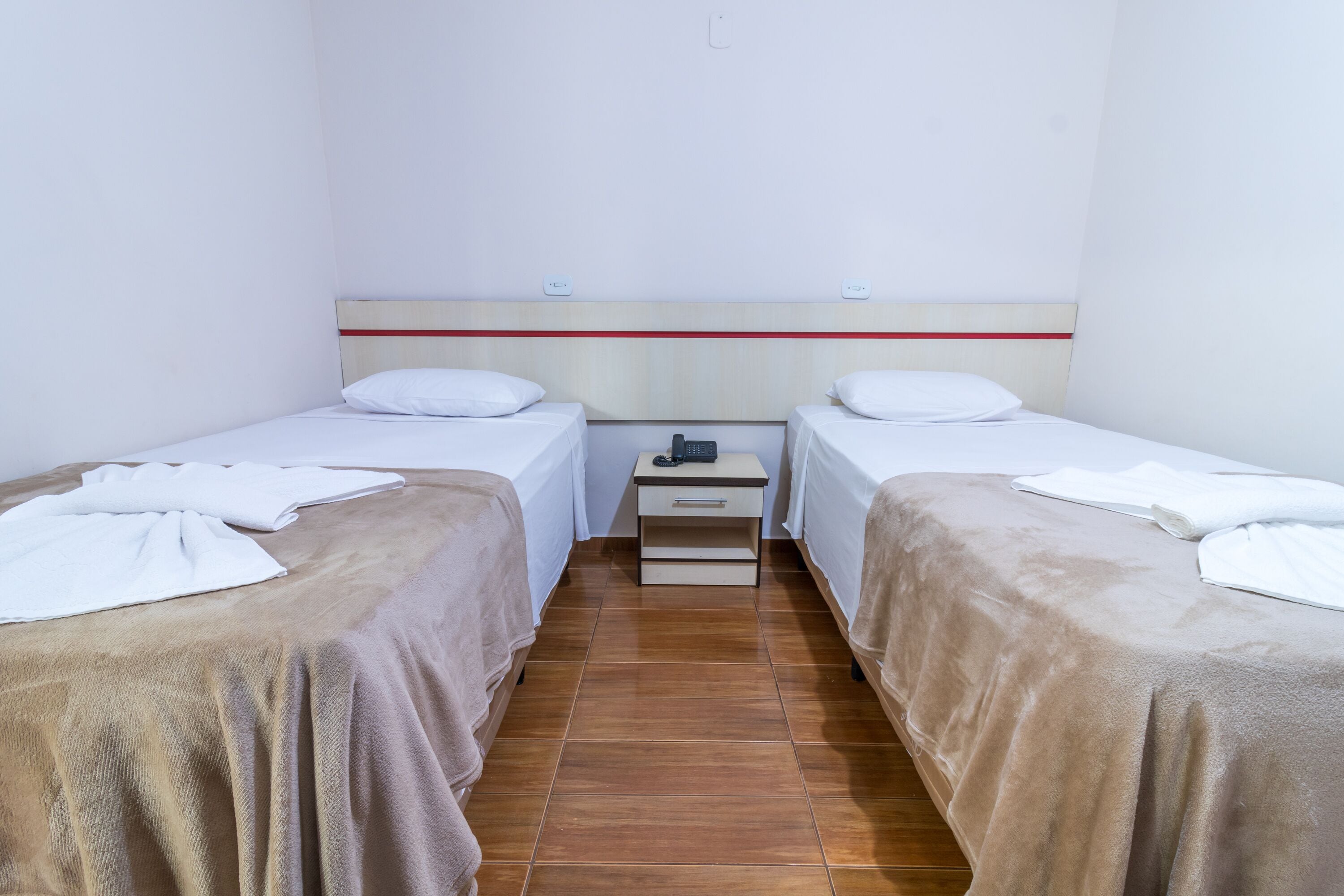 Een kamer met twee eenpersoonsbedden, een klein nachtkastje met een telefoon, en een wandlamp.