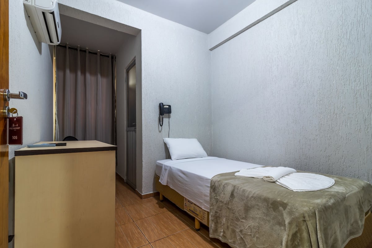 Ein kleiner, sauberer Raum mit einem Bett, einem Schreibtisch und einem Telefon an der Wand.