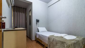 Quarto pequeno e limpo com uma cama, uma escrivaninha e um telefone na parede.