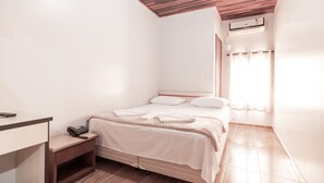 A bedroom with a wooden ceiling, a bed with white bedding, a bedside table with a phone, and an air conditioning unit on the wall. - Foz Fronteira Hotel (Foz do Iguaçu)