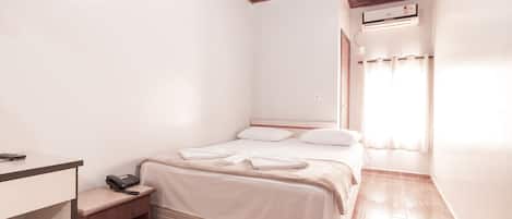 Ein Schlafzimmer mit Holzboden, einem Bett mit weißer Bettwäsche, einem Nachttisch mit Telefon und einer Klimaanlage an der Wand.