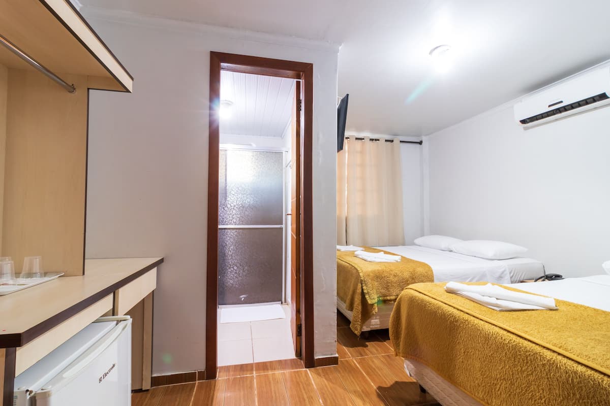 Ein Hotelzimmer mit einem Holztisch, einem Bett mit gelber Bettdecke und einem weiteren Bett mit weißer Bettwäsche.