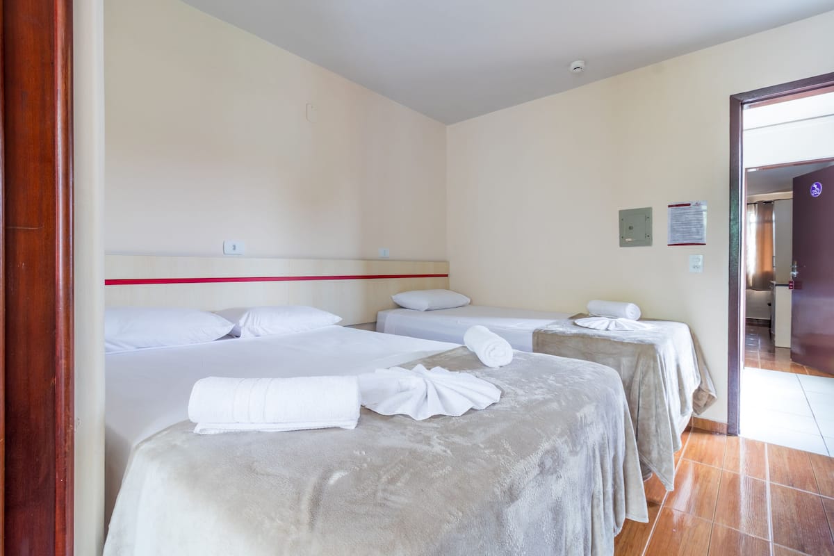 Ein Hotelzimmer mit zwei Betten, jeweils mit weißer Bettdecke und gerolltem Handtuch. Links ist ein Holztürrahmen und der Boden ist mit Fliesen belegt.