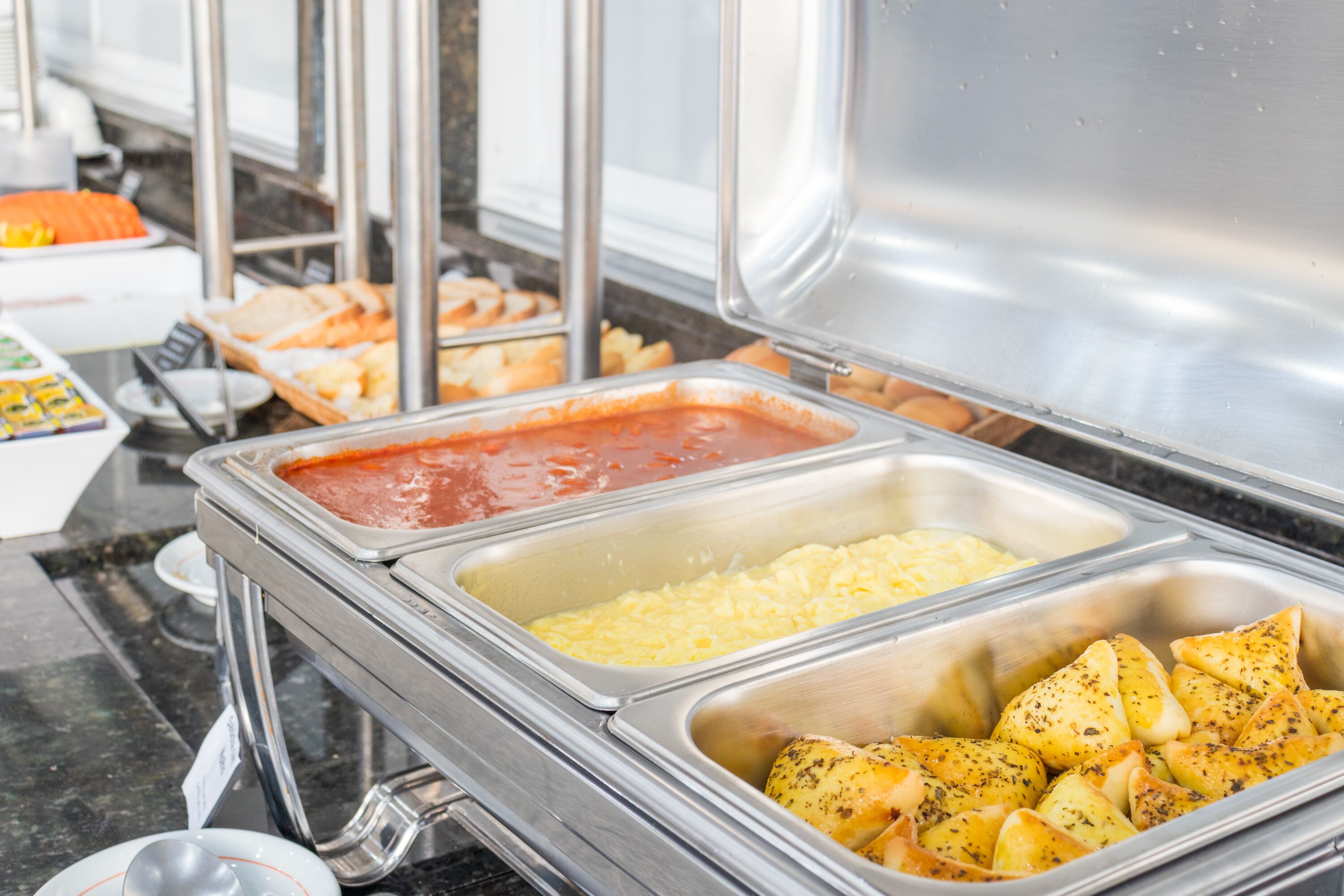 A buffet with various food items including scrambled eggs, potatoes, and a tomato-based sauce.