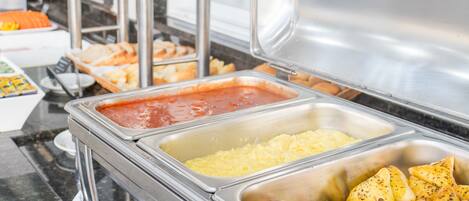 A buffet with various food items including scrambled eggs, potatoes, and a tomato-based sauce.