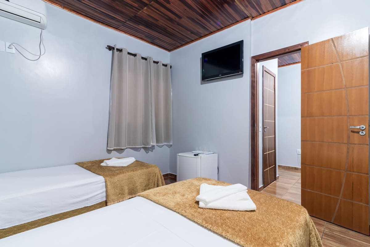 Ein Hotelzimmer mit zwei Betten, einem an der Wand befestigten Fernseher, einer Holztür und einem kleinen Nachttisch.