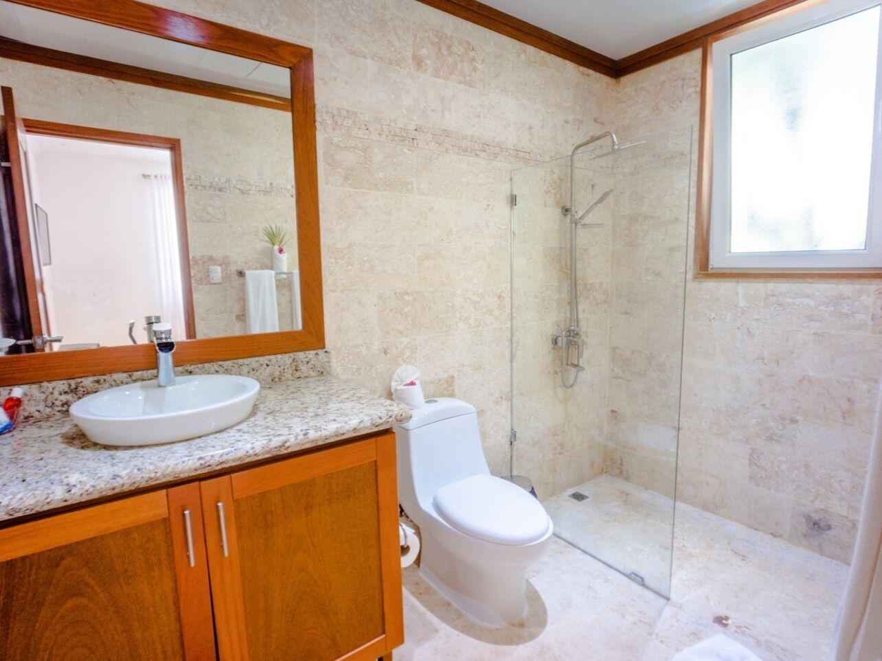 Un baño con lavamanos de mármol, armarios de madera, inodoro blanco y cabina de ducha de vidrio.