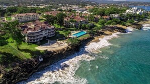A coastal resort with multiple buildings, a swimming pool, and a rocky shoreline.