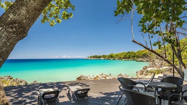 A wooden deck with outdoor furniture overlooking a turquoise sea and a clear sky.