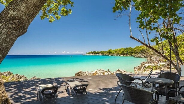 A wooden deck with outdoor furniture overlooking a turquoise sea. - Luxury Beachfront Condo - Hispaniola Beach 5B3 OceanView / 2 bed 2.5 bath (Sosúa)