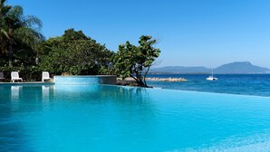 An infinity pool with clear blue water, white lounge chairs, and a view of the sea and distant mountains. - Luxury Beachfront Condo - Hispaniola Beach 5B3 OceanView / 2 bed 2.5 bath (Sosúa)