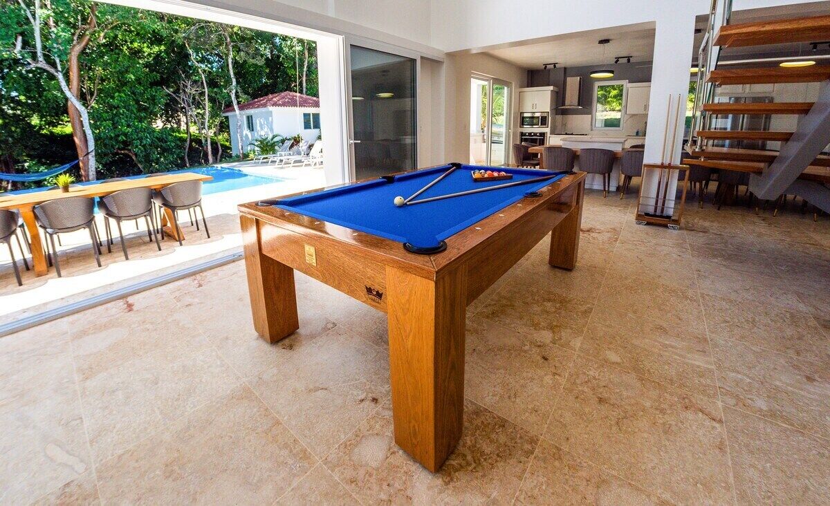 A pool table in a spacious room with a view of a swimming pool and outdoor seating.