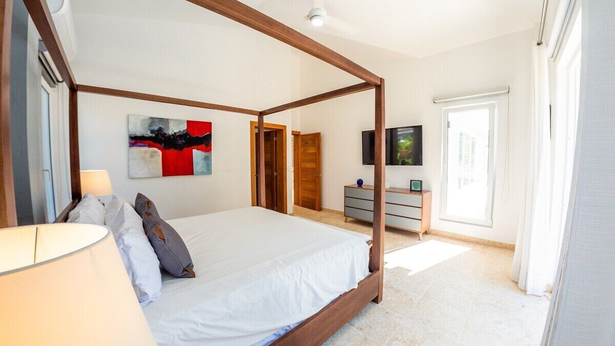 Une chambre à coucher avec un lit à baldaquin, un téléviseur à écran plat, un tableau au mur et une porte donnant sur une autre pièce.
