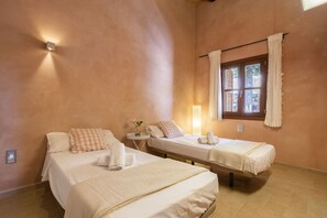 Een kamer met twee bedden, een klein tafeltje met een lamp en een raam met gordijnen.