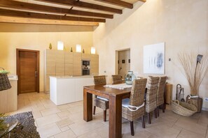 A modern kitchen with wooden cabinets, a central island, and a dining area with wicker chairs and a wooden table. - 3 bedroom villa with private pool (Mancor de la Vall)