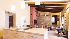 A kitchen with a large island, wooden beams, stone wall, and wicker furniture. - 3 bedroom villa with private pool (Mancor de la Vall)