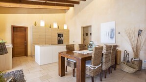 A modern kitchen with wooden cabinets, a central island, and a dining area with wicker chairs and a wooden table. - 3 bedroom villa with private pool (Mancor de la Vall)