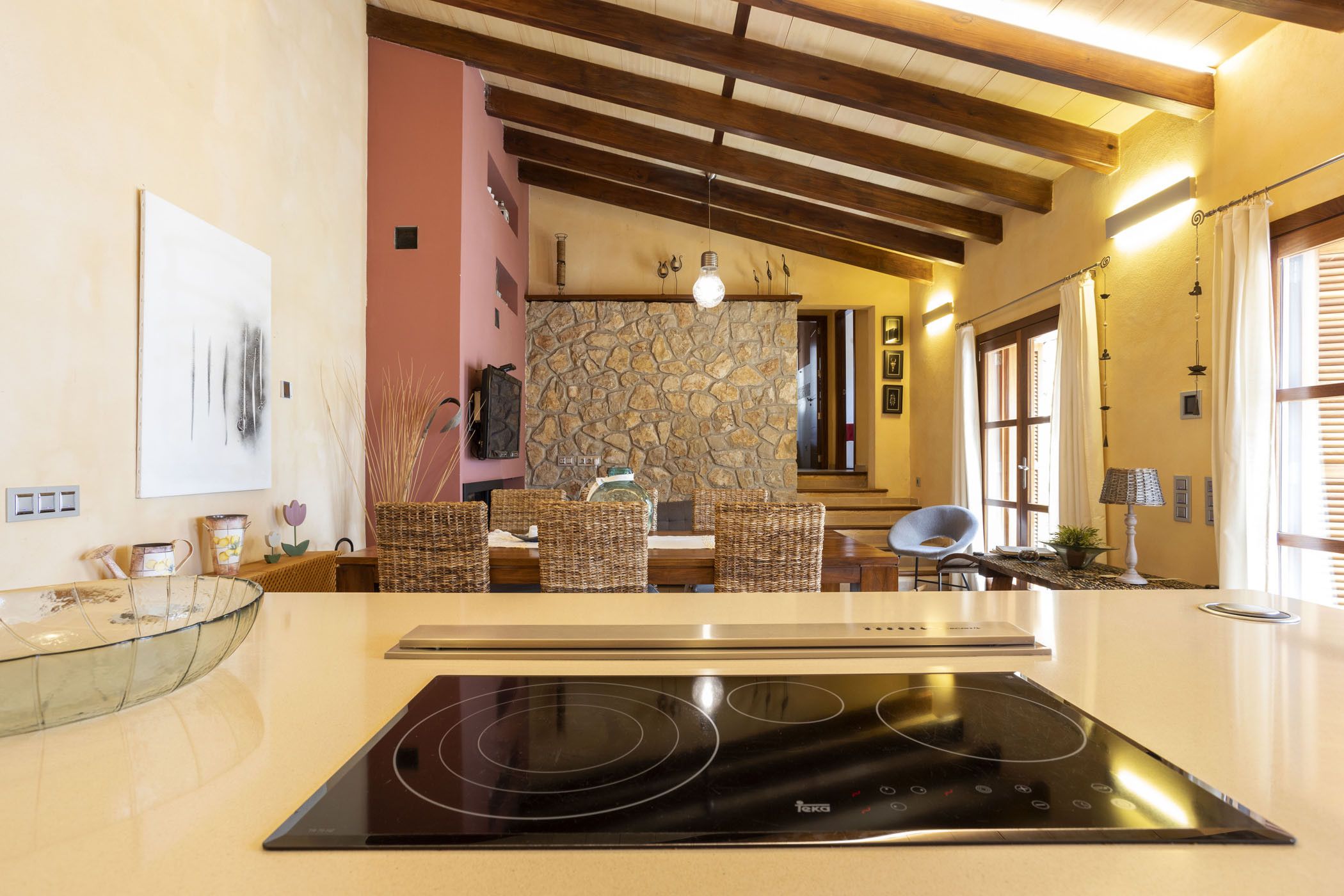 Una cocina moderna con placa de inducción integrada, salpicadero de pared de piedra y comedor con sillas de mimbre.
