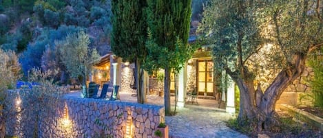 A stone-walled outdoor area with a seating arrangement and a building with a glass door.