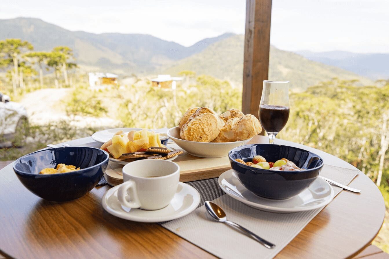 A table with breakfast items, a glass of red wine, and a scenic mountain view.