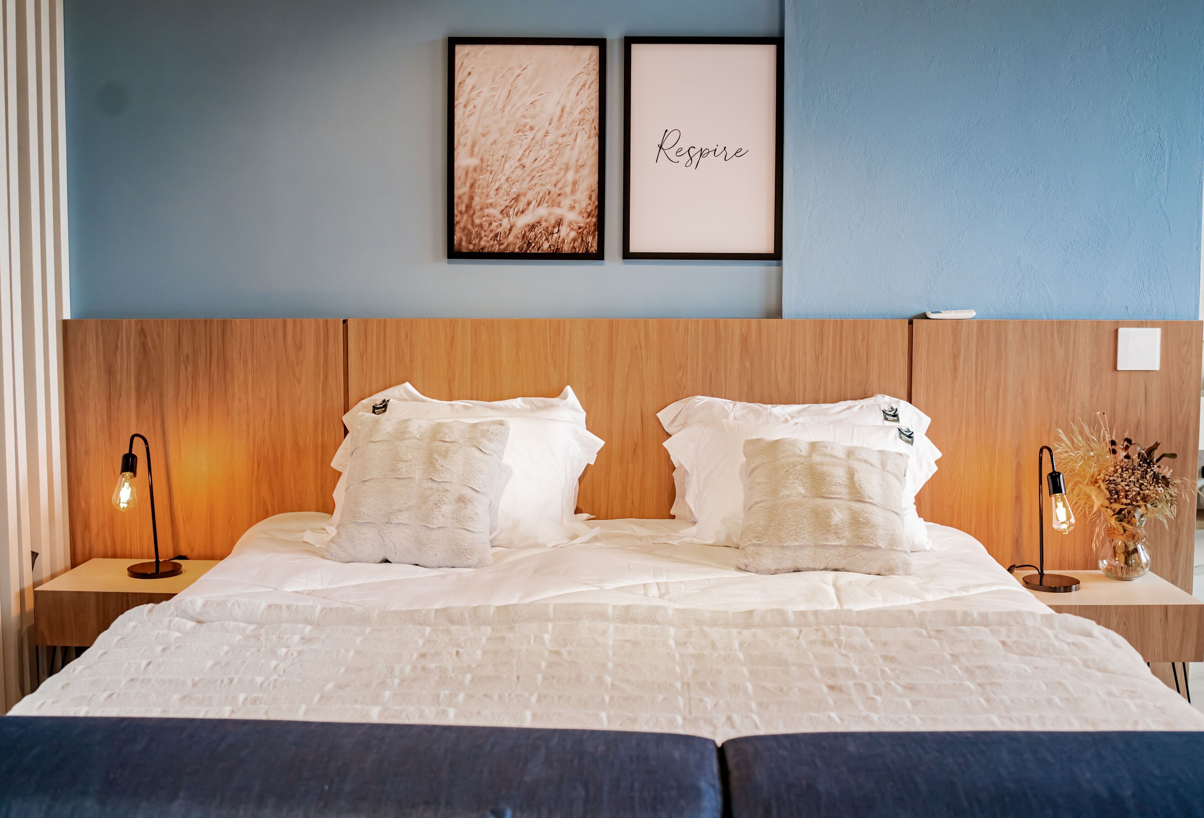 A neatly made bed with white bedding and two pillows, a wooden headboard, and two bedside tables with lamps.