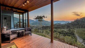 A modern outdoor seating area with a wooden deck, a sofa, and a small table, overlooking a mountainous landscape during sunset. - Parador do Rei (Urubici)
