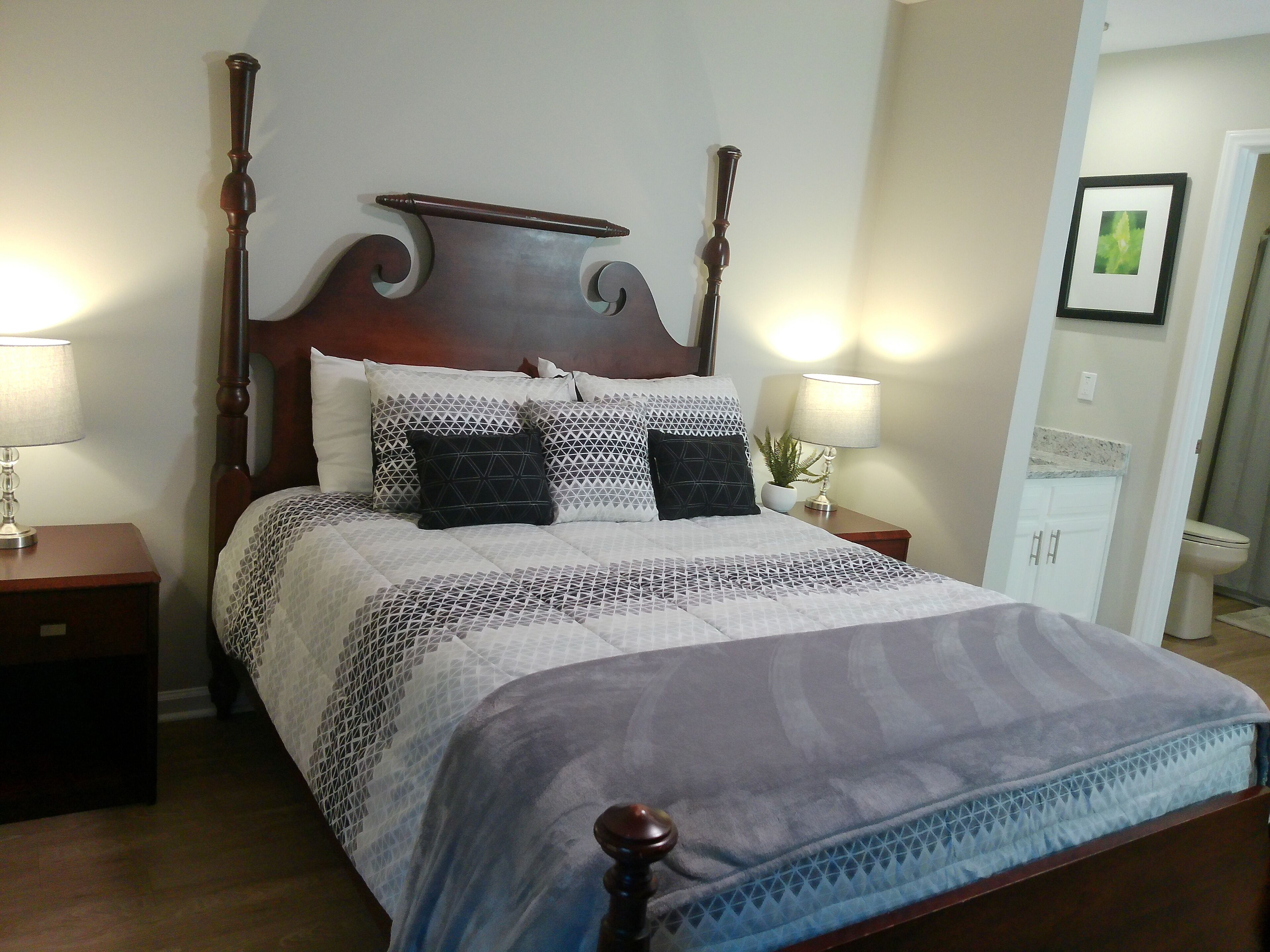 Een hemelbed met een houten hoofdeinde, meerdere kussens en twee nachtkastjes met lampen.