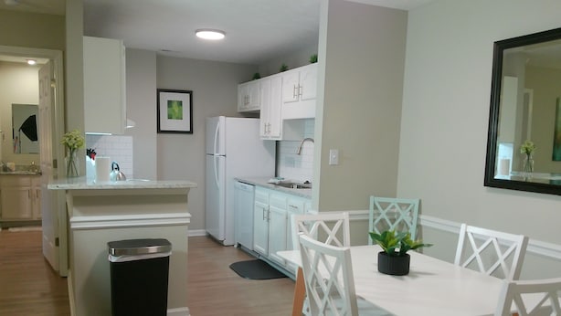 A modern kitchen with white cabinets, a refrigerator, and a dining area with white chairs and a table.