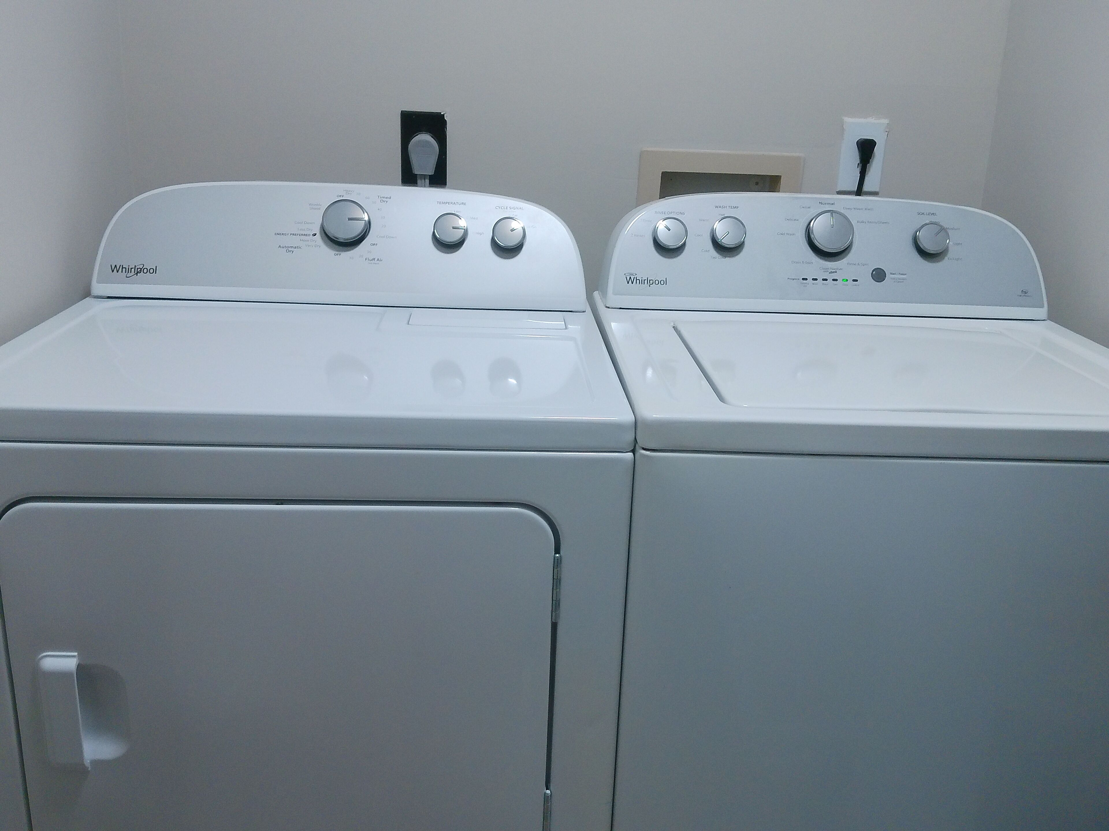 Due lavatrici Whirlpool bianche con caricamento frontale in una lavanderia, con una parete bianca e una porta sullo sfondo.