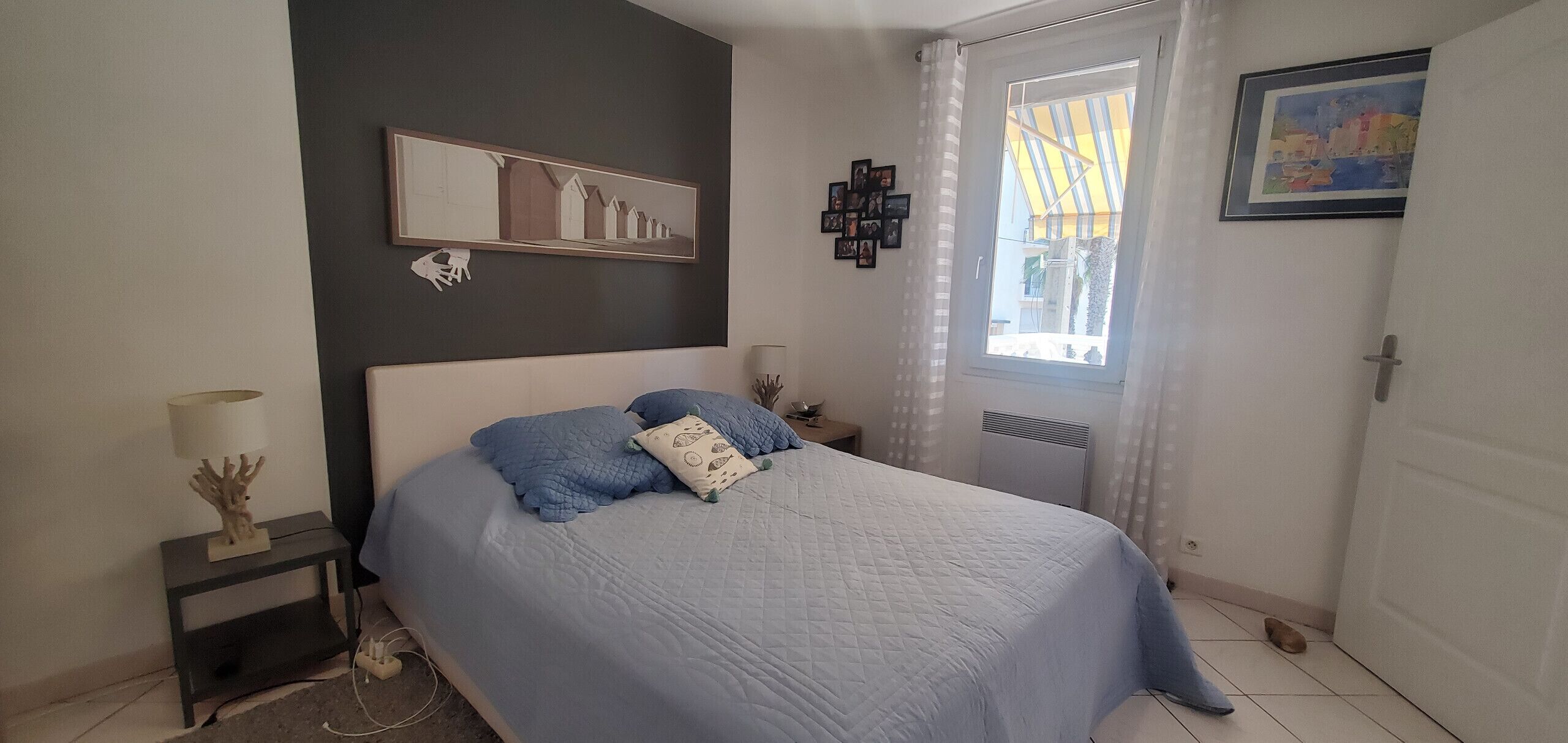 A bedroom with a bed, a nightstand, a lamp, a picture on the wall, and a window with curtains.