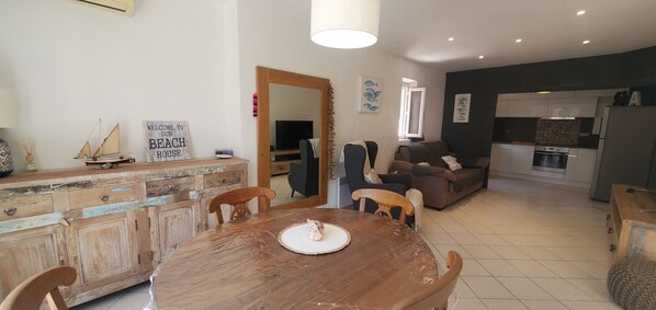 A cozy living room with a wooden dining table, a sofa, and a kitchen area with modern appliances. - Sea view and 50m from the beaches, 3-room apartment on the 1st floor of a villa, air-conditioned and a beautiful terrace for 4 privileged people (Fréjus)