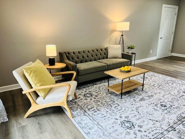 A living room with a sofa, armchair, coffee table, and patterned rug. - Corporate Rental in Merrillville (Merrillville)