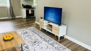 Ein modernes Wohnzimmer mit einem Flachbildfernseher auf einem weißen TV-Schrank, einem gemusterten Teppich und einem Holztisch.