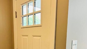 Eine beigefarbene Tür mit Fenster, Klingel und Lichtschalter an der Wand.
