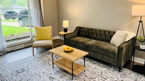 Ein Wohnzimmer mit Sofa, Sessel, Couchtisch, Lampe und Blick ins Freie.
