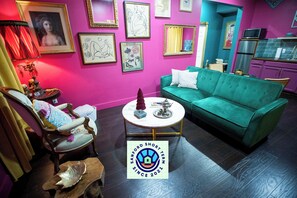 A vibrant living room with a teal sofa, a wooden chair, and a coffee table. - Boho Nights (Sanford)