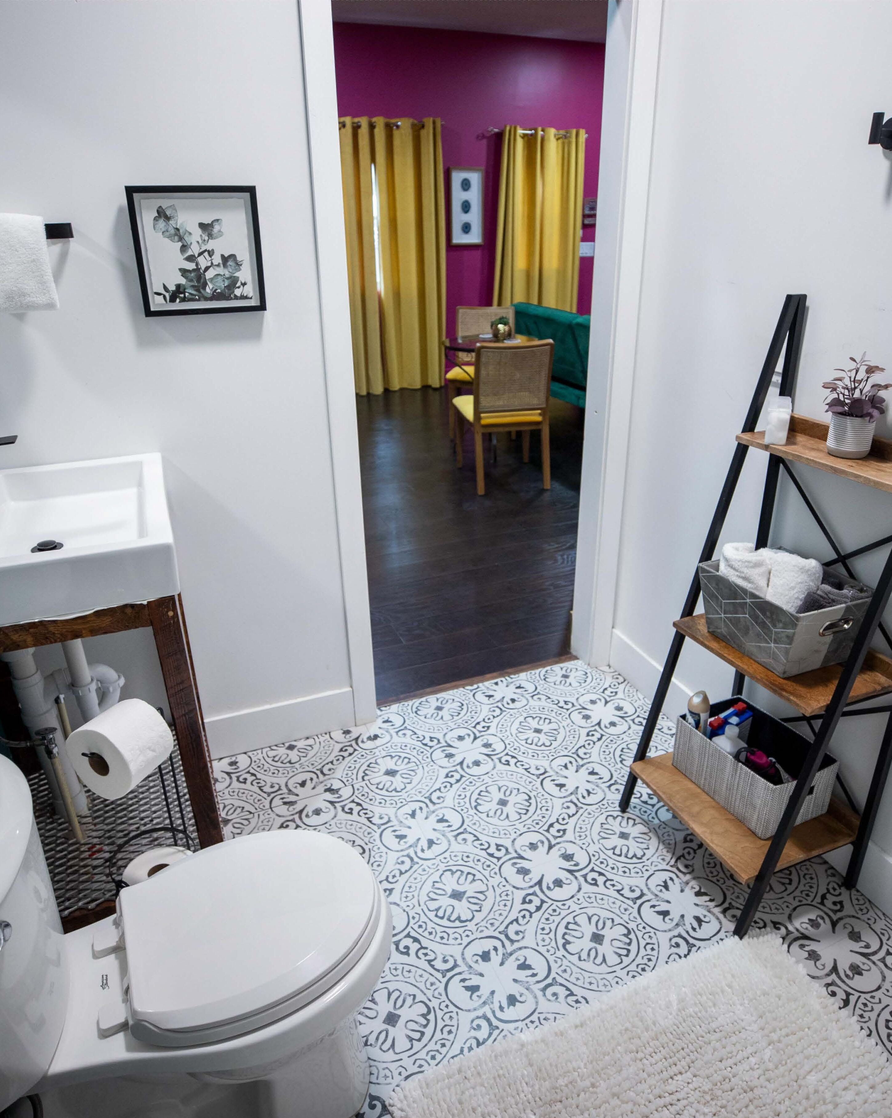 Une salle de bain avec des toilettes, un lavabo et un espace douche. On aperçoit une salle à manger à travers une porte ouverte au fond.