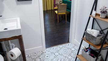 Une salle de bain avec des toilettes, un lavabo et un espace douche. On aperçoit une salle à manger à travers une porte ouverte au fond.