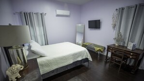 Une chambre d’hôtel équipée d’un lit, d’un bureau, d’un miroir, d’une télévision et d’une petite table agrémentée d’objets décoratifs.