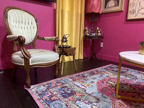 A room with a tufted armchair, a small wooden table, a patterned rug, and a framed picture on the wall. - Boho Nights (Sanford)