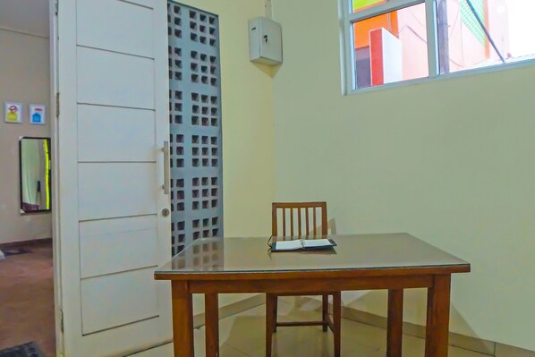 A room with a wooden table, a chair, a window, and a door with a metal grille.
