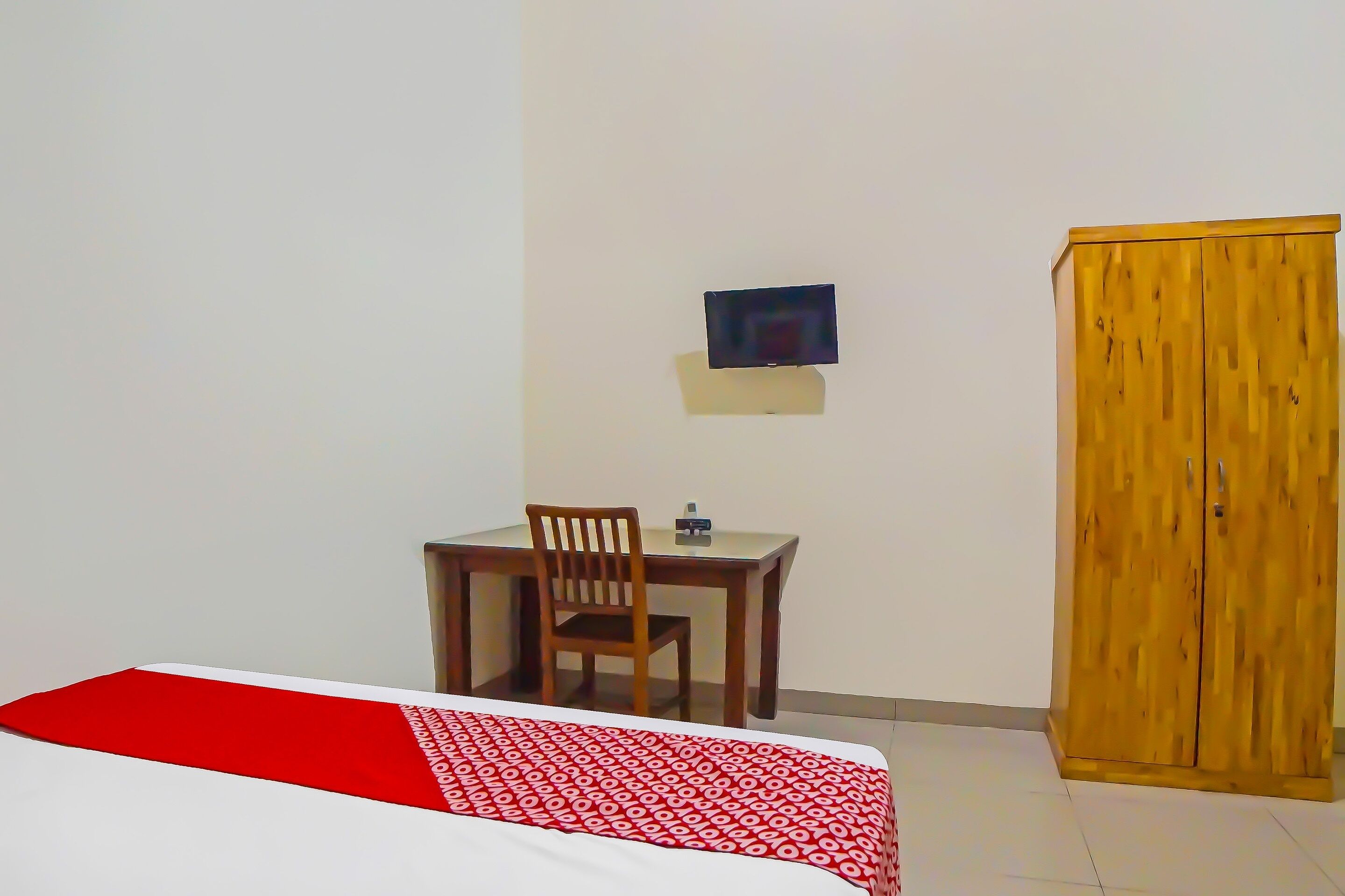 Un dormitorio con cama, un armario de madera, un escritorio con silla y un televisor pequeño de pared.