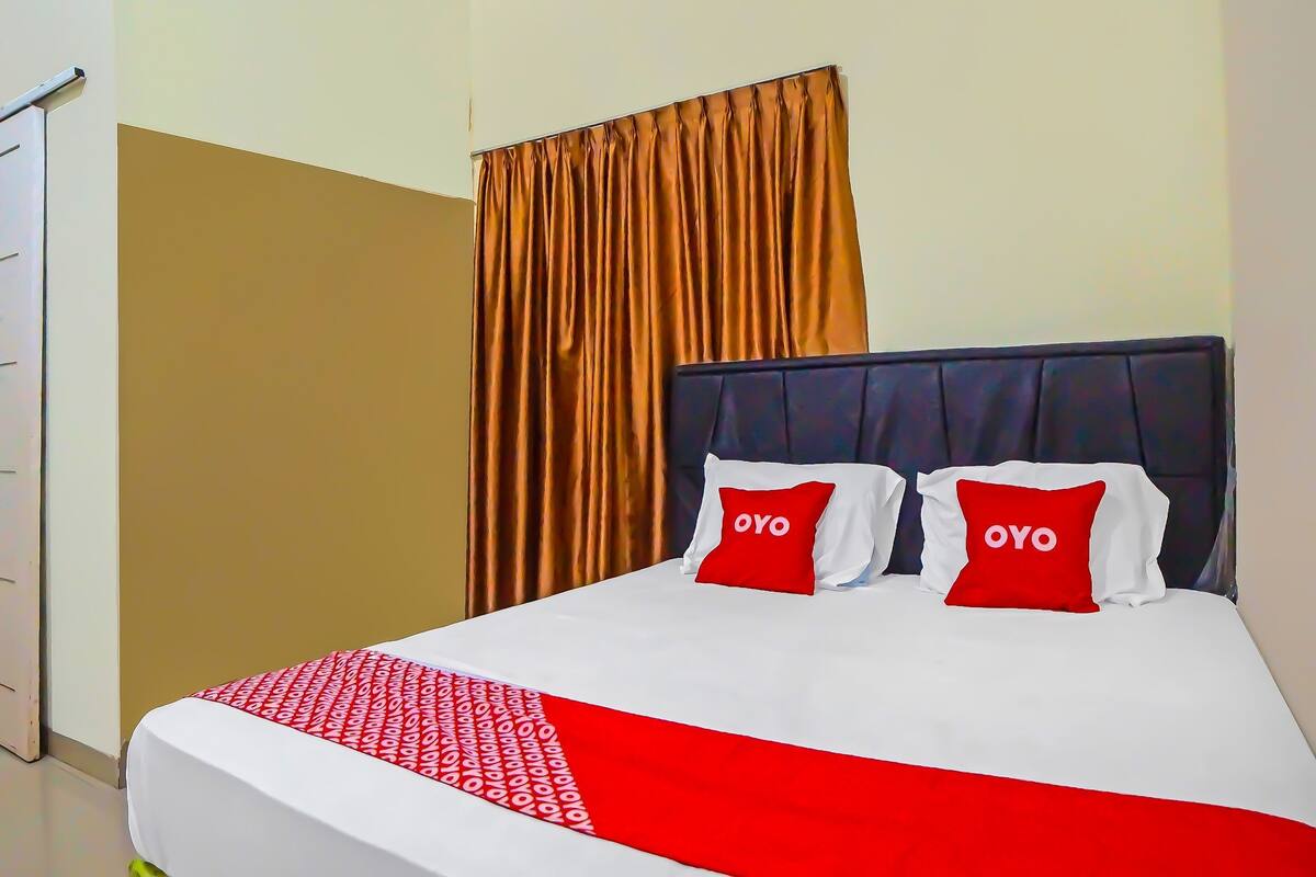 Hotelkamer met een bed, twee rode kussens met "OYO" erop, een rood-wit dekbed en een bruin gordijn.