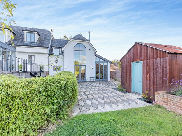 A residential property with a paved patio, a conservatory, and a fenced garden area.