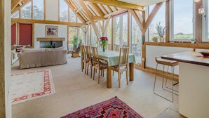 A spacious room with a high ceiling, wooden beams, a dining area with a table and chairs, a sofa, and a fireplace. - 5 bedroom accommodation in Martinstown, near Dorcester (Martinstown, near Dorcester)