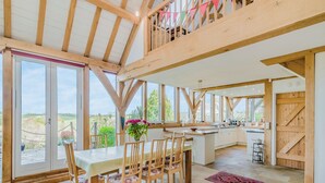 A spacious dining area with a large table and chairs, a kitchen in the background, and large windows offering a view of the outdoors. - 5 bedroom accommodation in Martinstown, near Dorcester (Martinstown, near Dorcester)