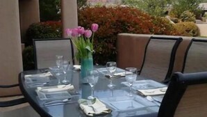 Un espace de restauration en plein air avec une table en verre prévue pour quatre personnes, entourée de chaises.