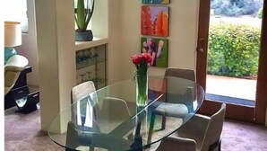 Un coin repas avec une table et des chaises en verre, un vase rempli de fleurs et des œuvres d’art colorées accrochées au mur.