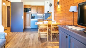 A compact kitchen with wooden cabinets, a dining table with chairs, a microwave, and a coffee maker. - Apt 4 ppl, balcony, near the ski runs (Modane)
