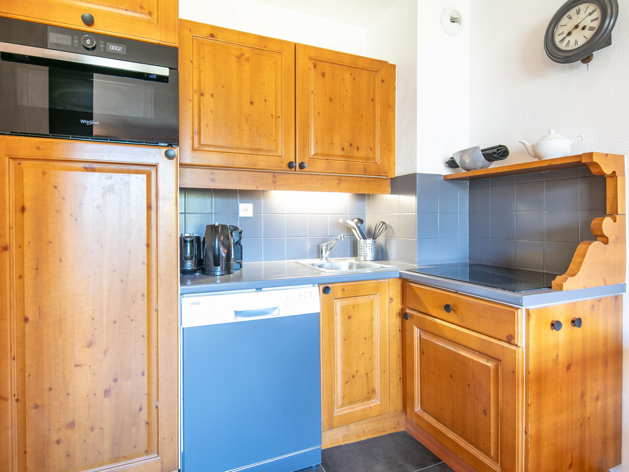 A kitchen with wooden cabinets, a built-in oven, a sink, and a clock on the wall.